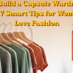 Women's fashion Pinterest pin titled "How to Build a Capsule Wardrobe on a Budget 7 Smart Tips for Women Who Love Fashion.webp". The banner shows bold yellow text at the top. The background features two clothing racks with minimalist outfits on wooden hangers. In the foreground, grey, sage green, and terracotta clothes are lined up. On the right, a smaller vertical insert shows a close-up of a rust-brown blouse, a striped tee, and linen shirts, highlighting affordable capsule wardrobe pieces.
