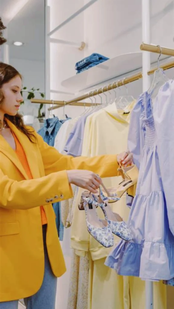 Pinterest pin titled "Keeping Your Capsule Fresh and Functional.webp". The image shows a woman in a vibrant yellow blazer browsing a clothing rack filled with light-colored, breezy apparel and floral footwear. This pin offers guidance on how to maintain the versatility of your **Capsule Wardrobe** while keeping your style feeling new and exciting. It demonstrates that a thoughtful, edited approach to fashion can remain fresh, seasonal, and perfectly tailored to your individual aesthetic.
